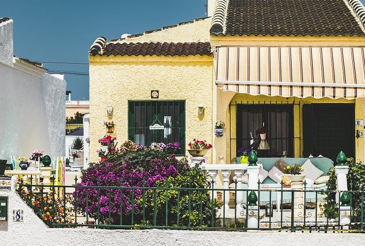 Terrassengestaltung im mediterranen Stil Bild zeigt gelbes Haus mit Veranda, Markise und blauem Sofa